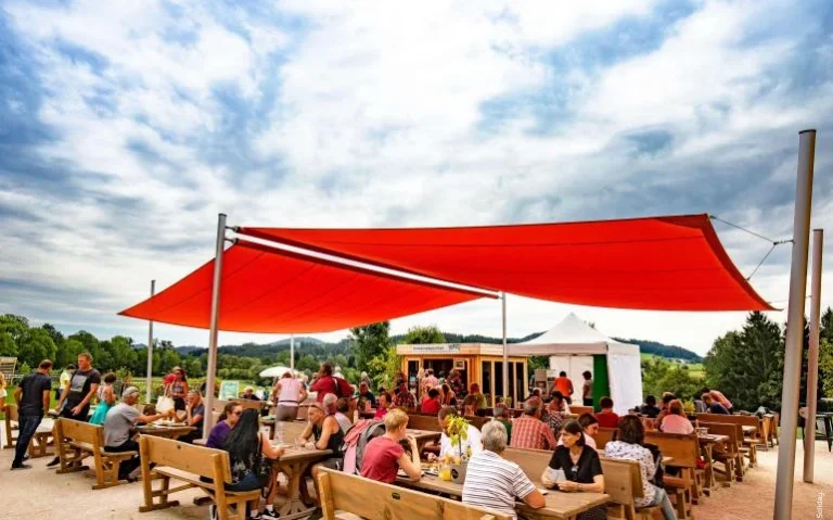 Červená stínicí plachta nad restaurační zahrádkou